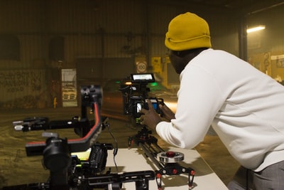 Yellow knitted cap, wearing a white long sleeve shirt and holding a black camera
